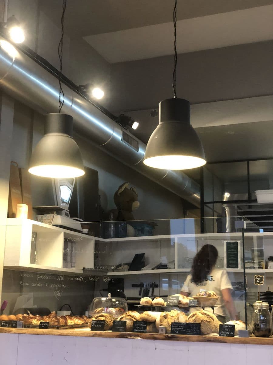 Interior do café 55: balcão com pães de massa mãe, candeeiros pretos e a equipa ao trabalho